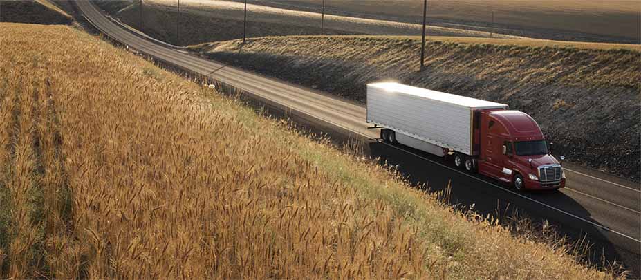 Semi truck driving down a road with fields on both sides.